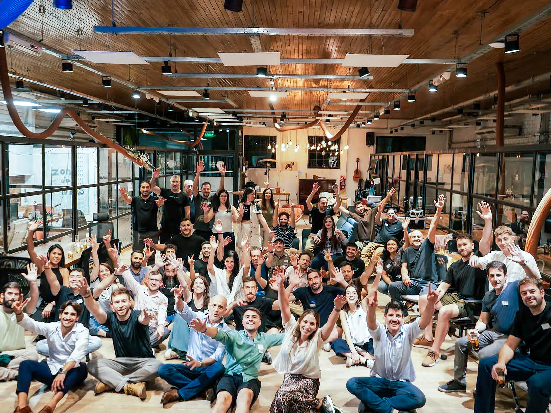 A full team gathered in a coworking space at the end of an offsite, arms raised for a group photo
